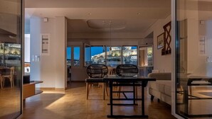 A modern interior with a dining area featuring a wooden herringbone floor, two black chairs, and a glass partition. - Unique 2BR Penthouse with Stunning Acropolis View (Athens)