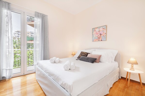 A hotel room with a bed, a nightstand, a lamp, a painting, and a view of the outside.