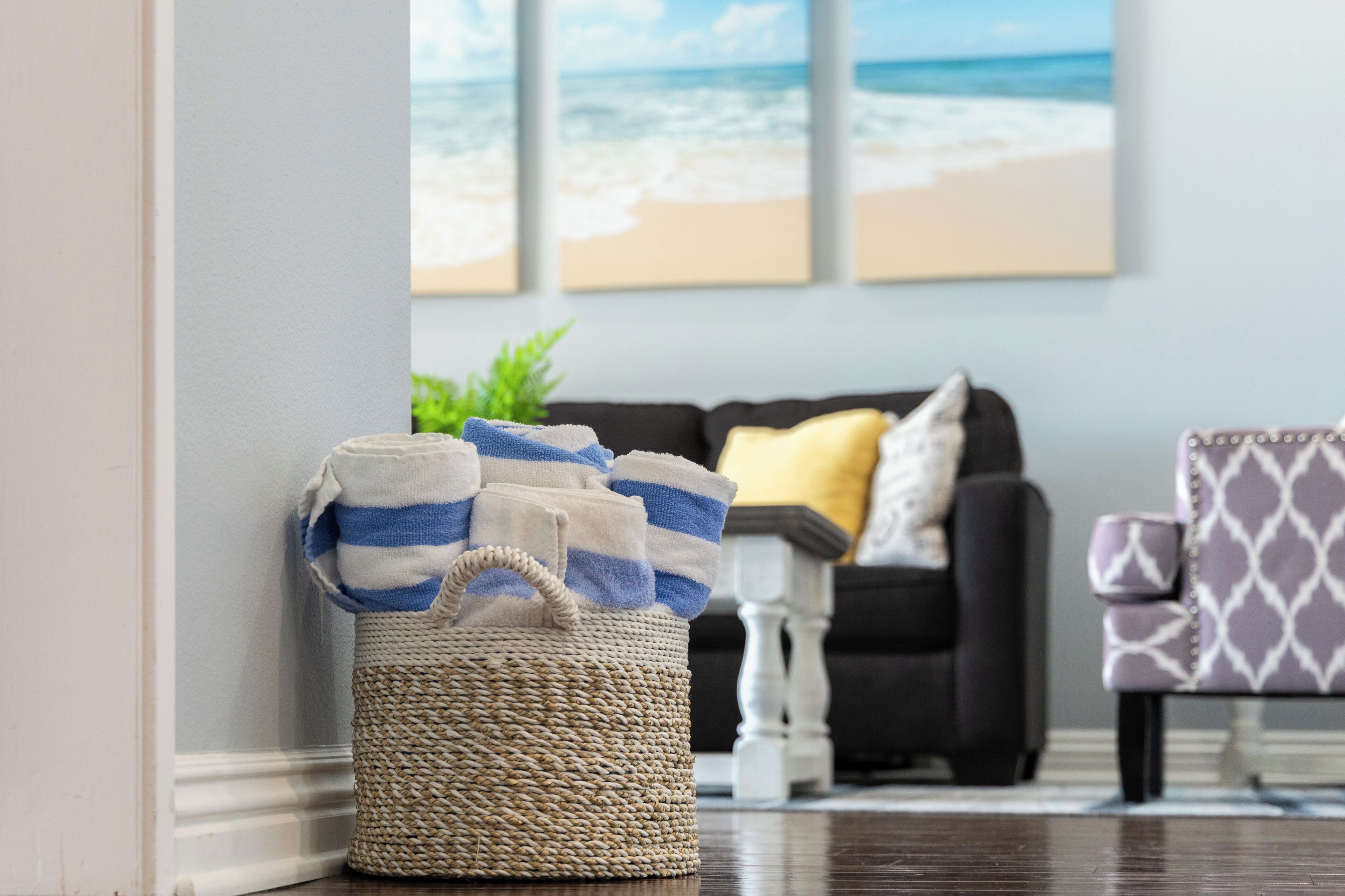 A living room with a woven basket filled with striped towels, a dark-colored sofa with a yellow pillow, and a patterned armchair.