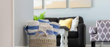 A living room with a woven basket filled with striped towels, a dark-colored sofa with a yellow pillow, and a patterned armchair.