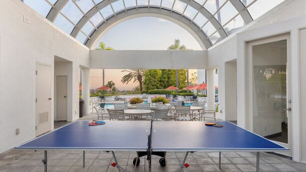 A ping pong table in a covered outdoor area with a glass ceiling, surrounded by chairs and tables, overlooking a pool area. - Encantamar Escape by AvantStay | Prime Location + Community Amenities (Dana Point)