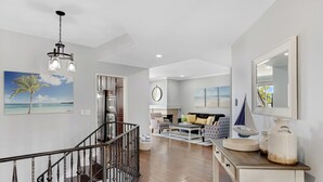 A spacious living area with a wooden floor, a staircase, a large mirror, and a painting of a beach scene. - Encantamar Escape by AvantStay | Prime Location + Community Amenities (Dana Point)