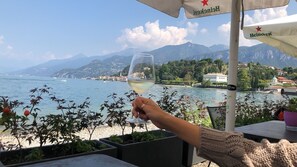 Une personne tenant un verre de vin, avec en arrière-plan un paysage pittoresque composé d’un lac et de montagnes.