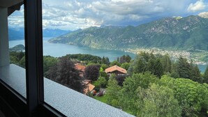 Vista des d'una finestra sobre un paisatge de muntanyes amb un llac i una vila.