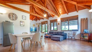 Un vaste espace de vie doté d’un plafond en bois, d’une table à manger avec des chaises, d’un canapé et d’un téléviseur.