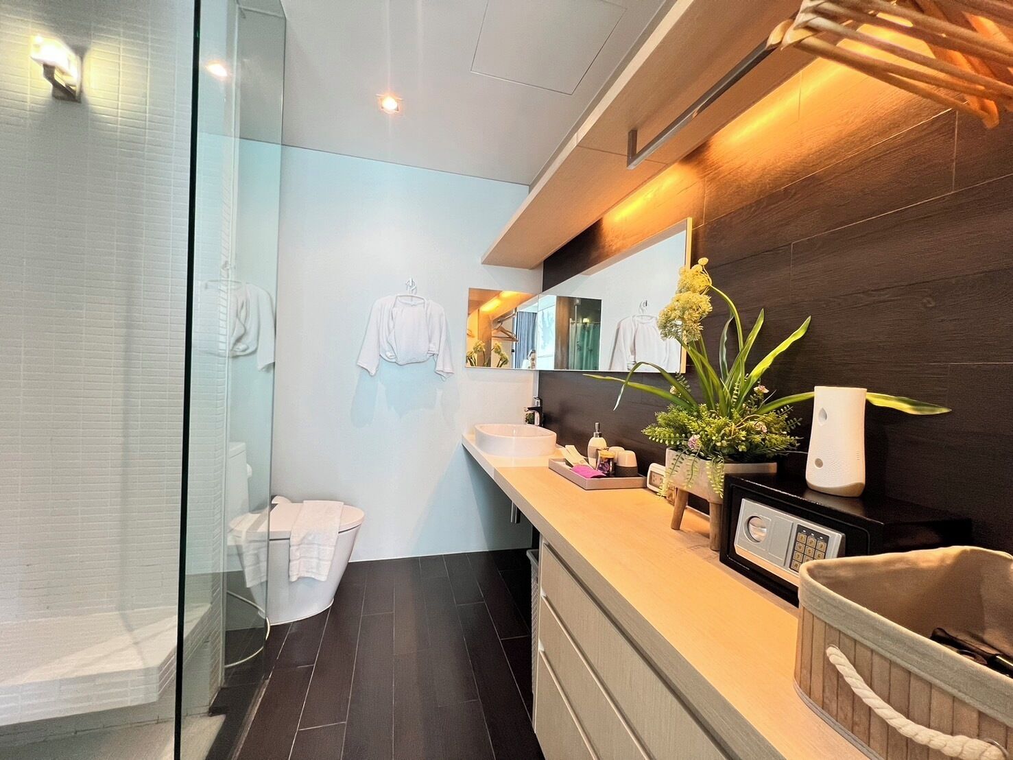 A modern bathroom with a glass shower enclosure, a white toilet, a sink with a mirror, and a plant on the counter.