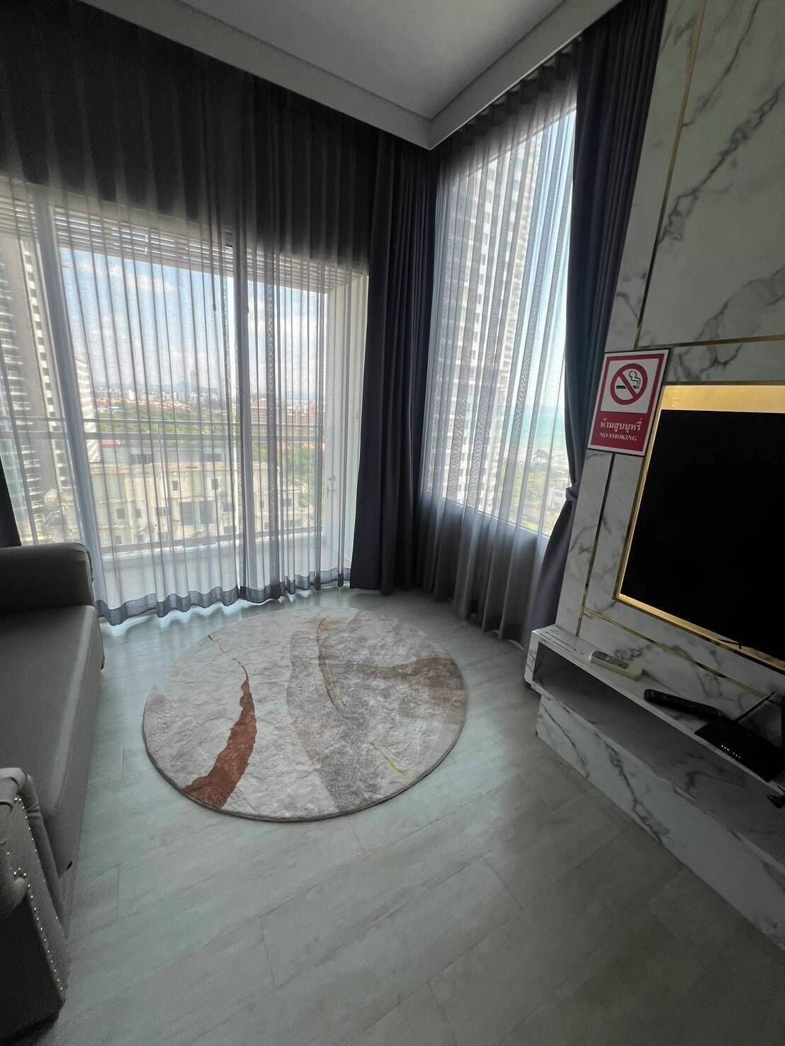 Een moderne woonkamer met een grote televisie, een open haard en stadszicht door dunne gordijnen.