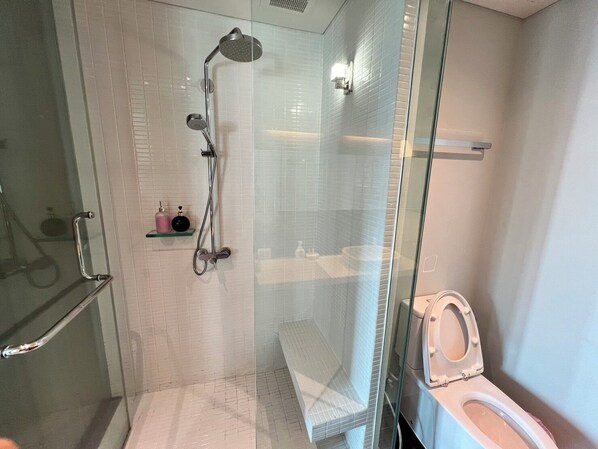 A modern bathroom with a glass-enclosed shower, a toilet, and a small shelf with toiletries. - Residence Veranda By Thita (Pattaya)