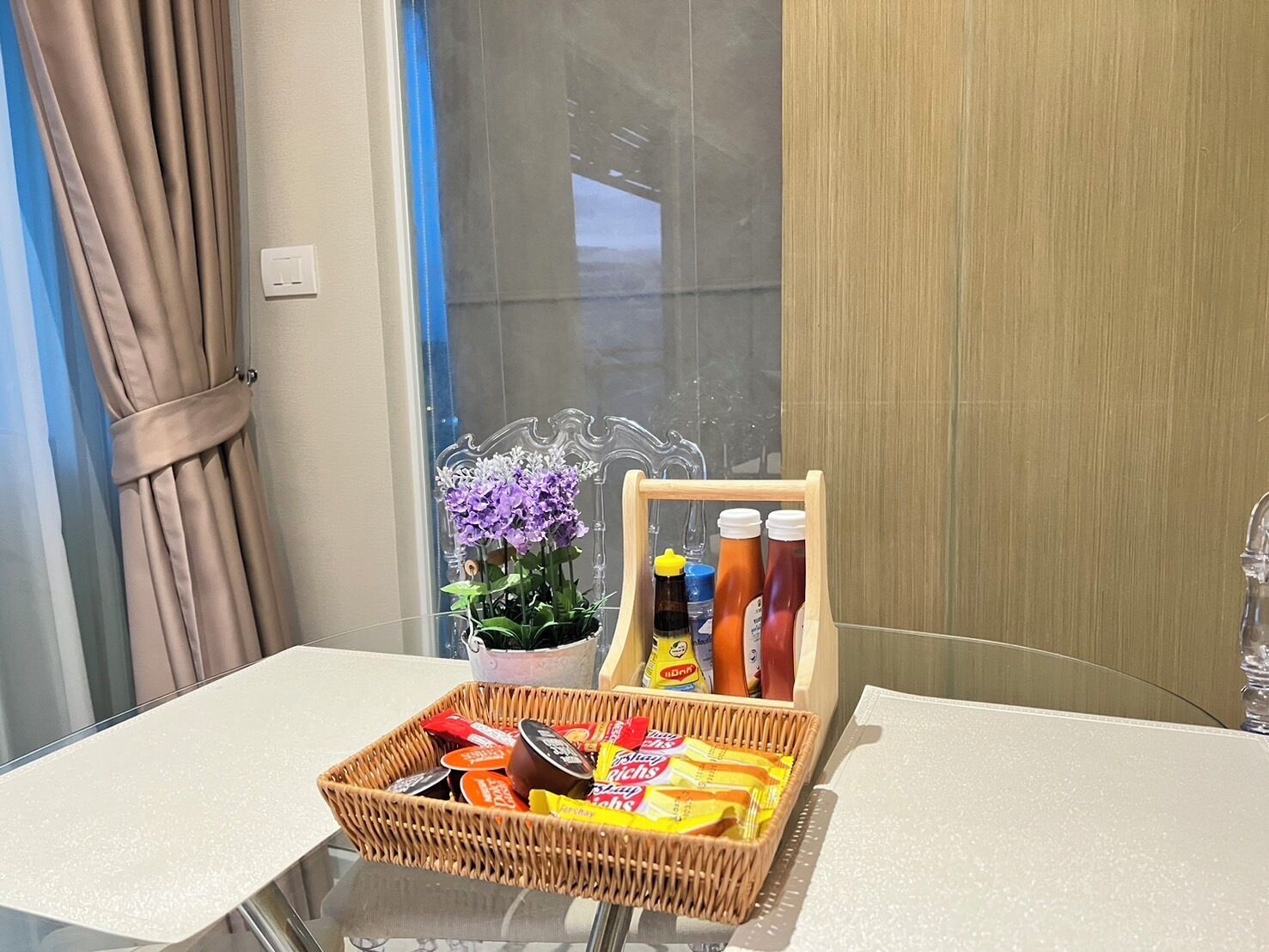 A hotel room with a table set with snacks, condiments, and a potted plant.