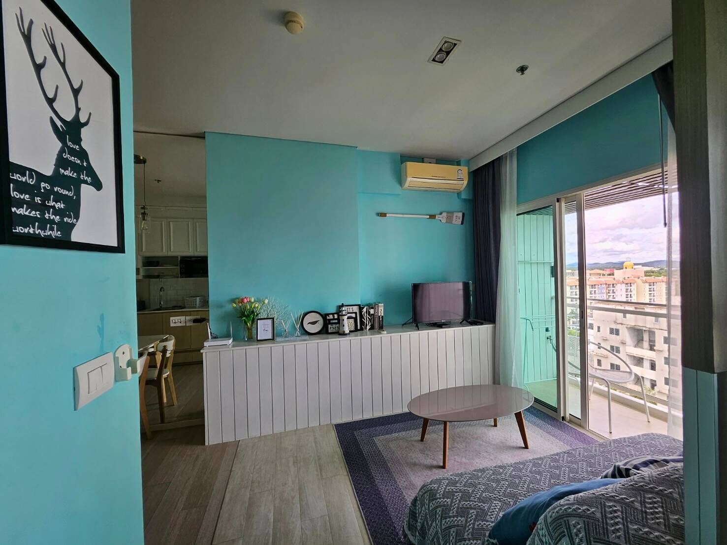 A modern living room with teal walls, a dining area, and a balcony with a city view.