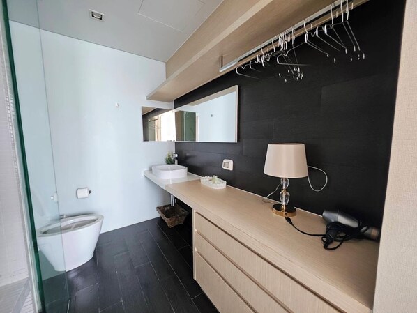 Une salle de bain moderne avec un grand miroir, un lavabo rond, un meuble-lavabo avec des tiroirs et un porte-vêtements suspendu.