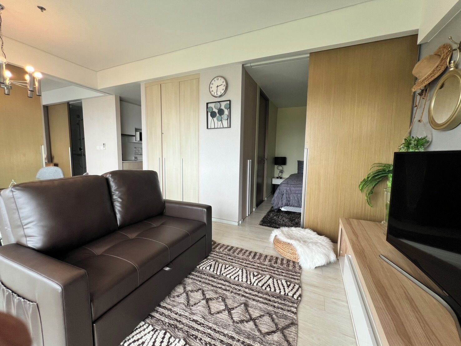 A modern living room with a brown leather sofa, a patterned rug, a flat-screen TV, and a wooden cabinet.