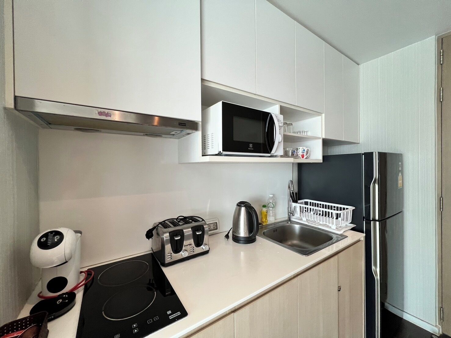 A compact kitchen with a microwave, toaster, kettle, and a stainless steel refrigerator.