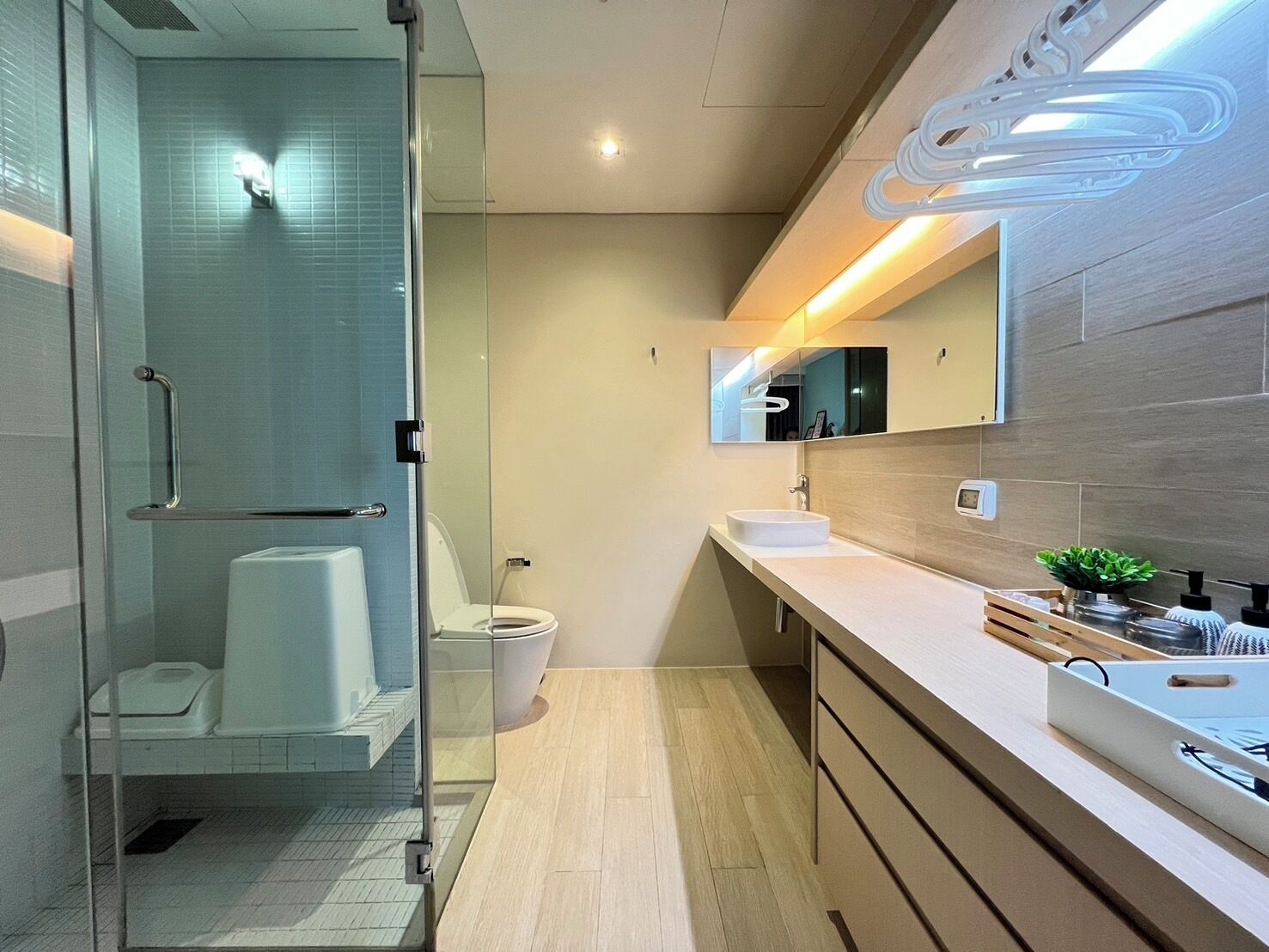 A modern bathroom with a glass shower enclosure, a toilet, a sink with a mirror, and wooden cabinets.