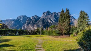 Ein Park mit einem gepflasterten Weg, der zu einer Rasenfläche führt, umgeben von Bäumen und einem Bergkamm im Hintergrund.