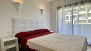 A bedroom with a white headboard, a red bedspread, and two wall-mounted lights. - JARDINS DEL MAR 127 (Estartit)