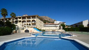 A swimming pool area with a building in the background, a lifeguard tower, and a mountain. - JARDINS DEL MAR 127 (Estartit)