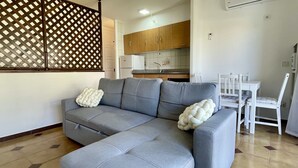 A modern living room with a grey sectional sofa, white throw pillows, and a dining area with a white table and chairs. - JARDINS DEL MAR 127 (Estartit)