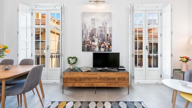 A modern living room with a cityscape painting, a flat-screen TV, and a wooden cabinet. - Solaga - Casapalma (Málaga)