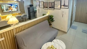 A modern living room with a sofa, a small round table with a vase, a TV mounted on the wall, and framed pictures on the wall. - Chic 1-bedroom apartment in brilliant Pasay with WiFi, AC (philippines)