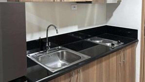 A modern kitchen with wooden cabinets, stainless steel sink, and black countertop. - Chic 1-bedroom apartment in brilliant Pasay with WiFi, AC (philippines)
