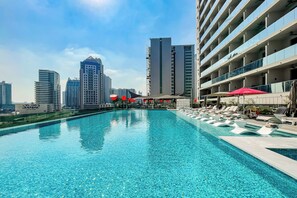 A swimming pool with lounge chairs and umbrellas, surrounded by high-rise buildings. - Executive Studio MAG 318 (Dubai)