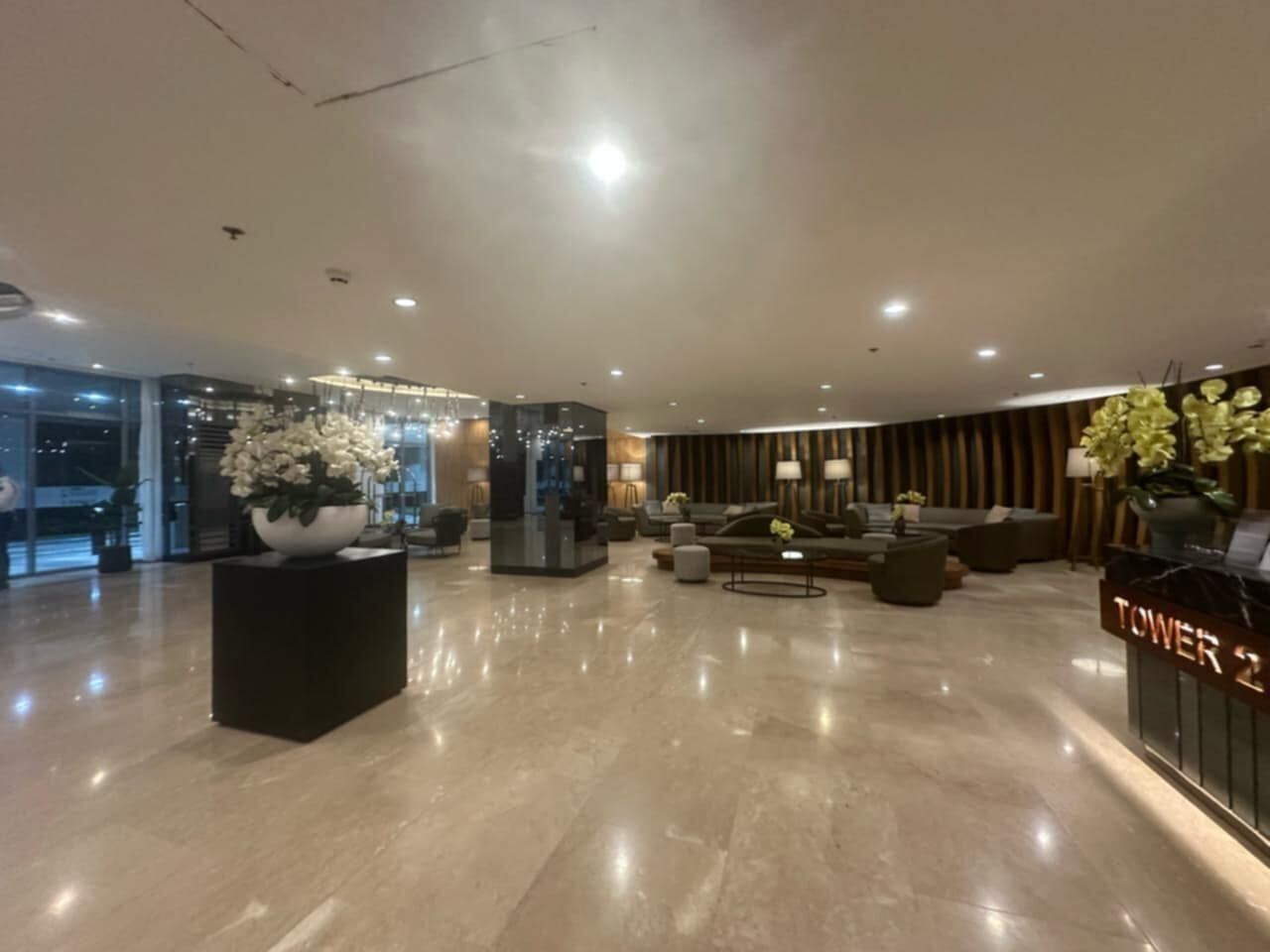 Un hall d’entrée spacieux avec un comptoir de réception, un espace salon et un grand vase rempli de fleurs.
