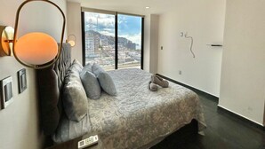 A modern bedroom with a large bed, a view of the city, and a unique wall-mounted lamp.