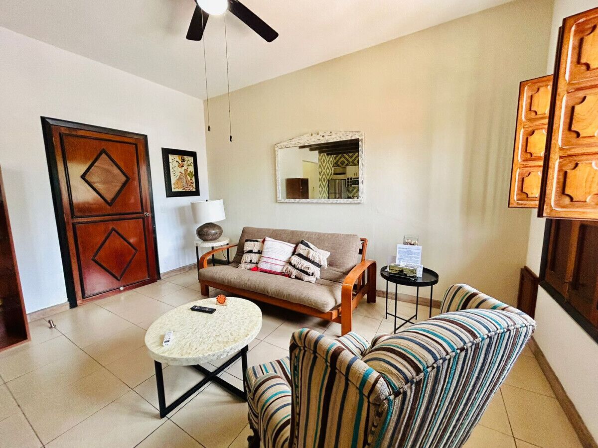 A living room with a sofa, armchairs, a coffee table, a lamp, and a mirror.