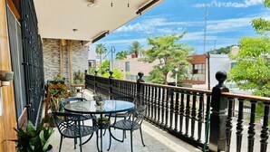 A balcony with a glass table and chairs, a black metal railing, and potted plants.