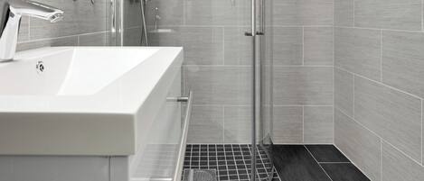 Un baño moderno con un lavamanos grande, cabina de ducha de vidrio y suelo de baldosas.