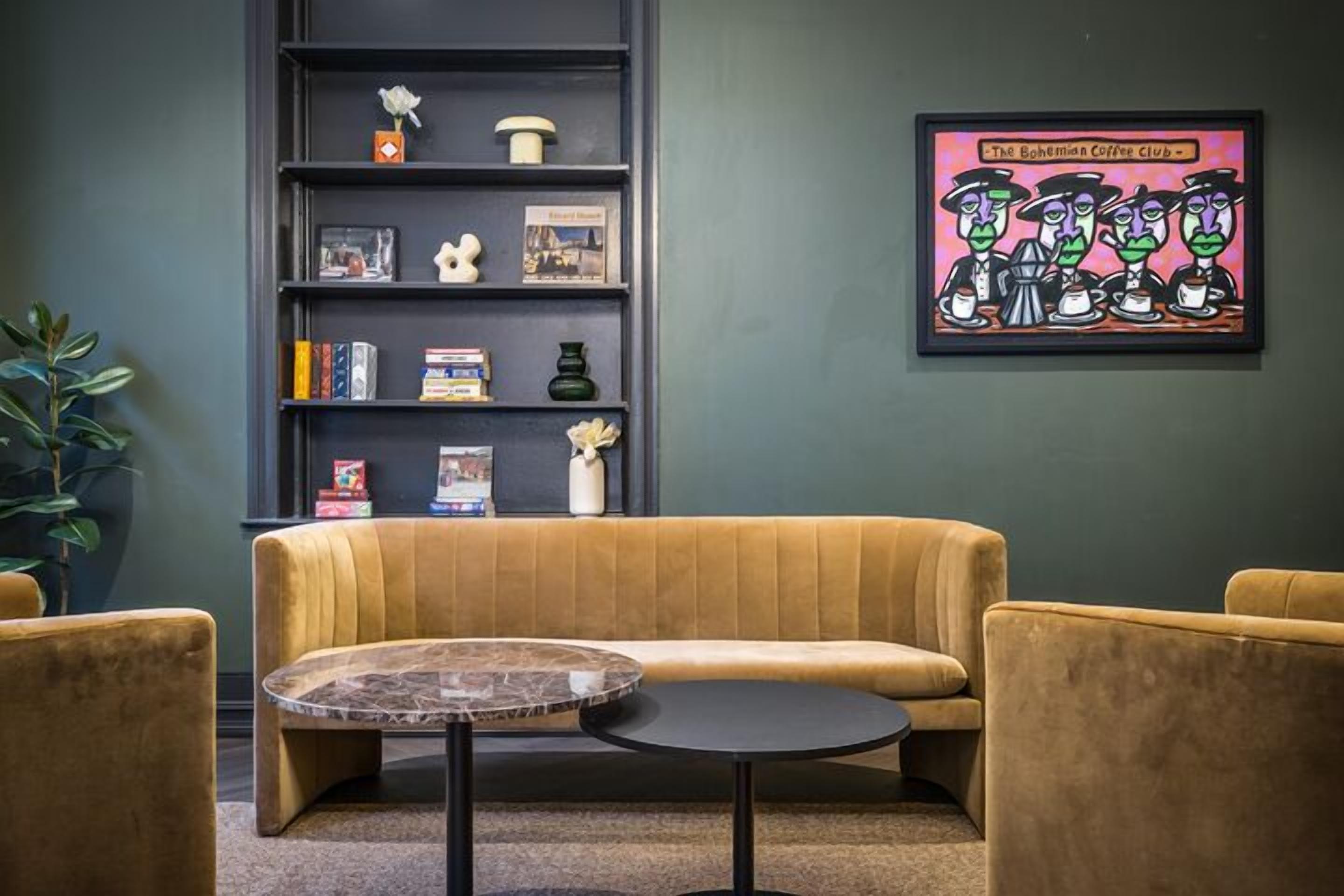 A cozy seating area with a sofa and two armchairs, a small round table, and a bookshelf with various items.