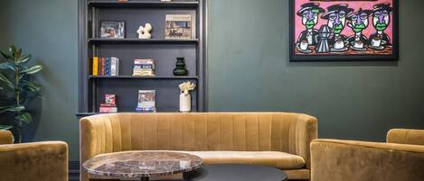 A cozy seating area with a sofa and two armchairs, a small round table, and a bookshelf with various items.