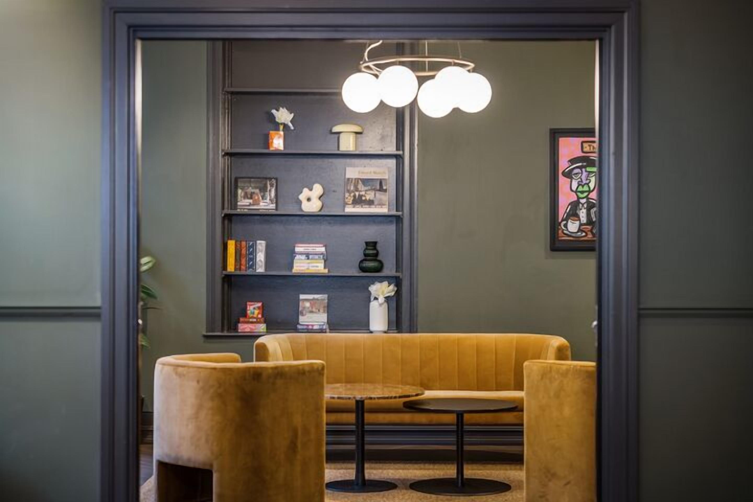Un interior moderno con un sofá y dos sillones, una estantería con diversos objetos y una lámpara de diseño único.