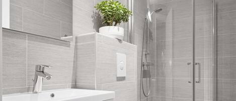 A modern bathroom with a white sink, mirror, and toilet, a glass shower enclosure, and a potted plant on a shelf.