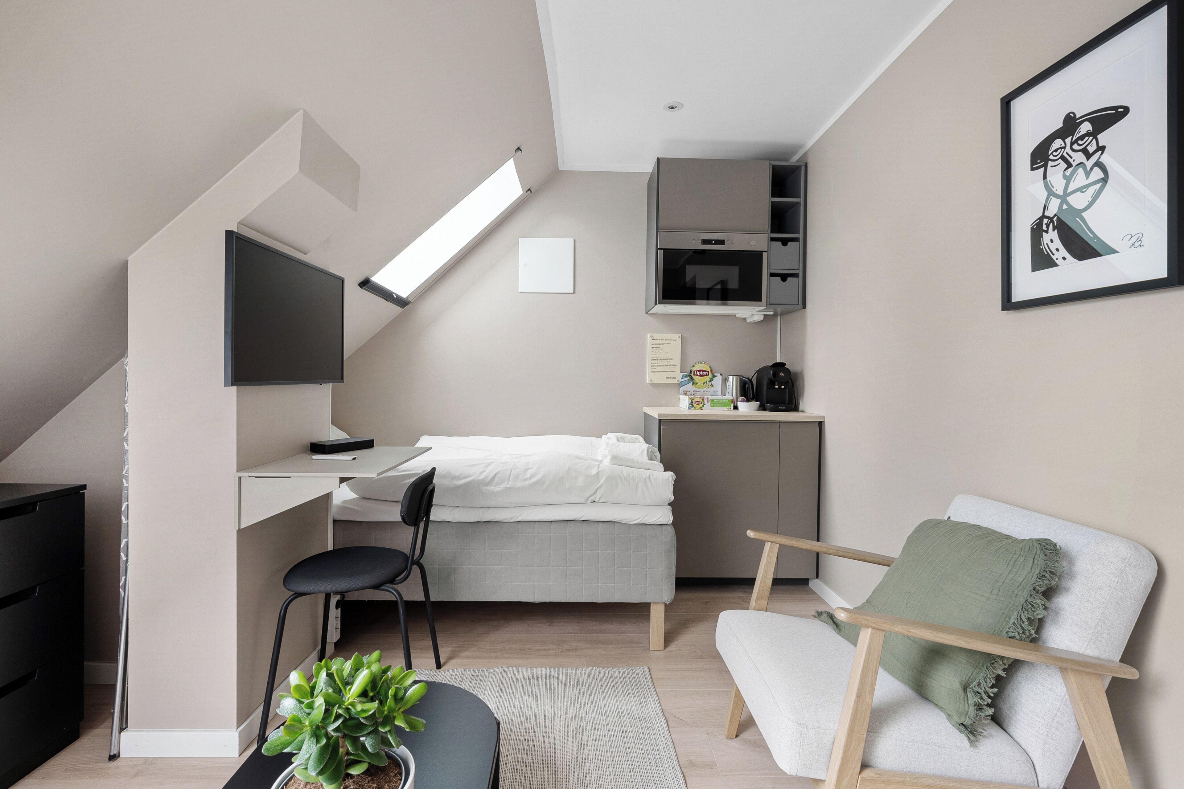 Un apartamento estudio pequeño con cama, escritorio, silla y kitchenette.