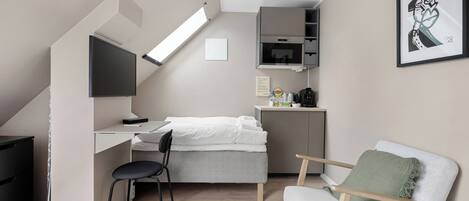 Un apartamento estudio pequeño con cama, escritorio, silla y kitchenette.