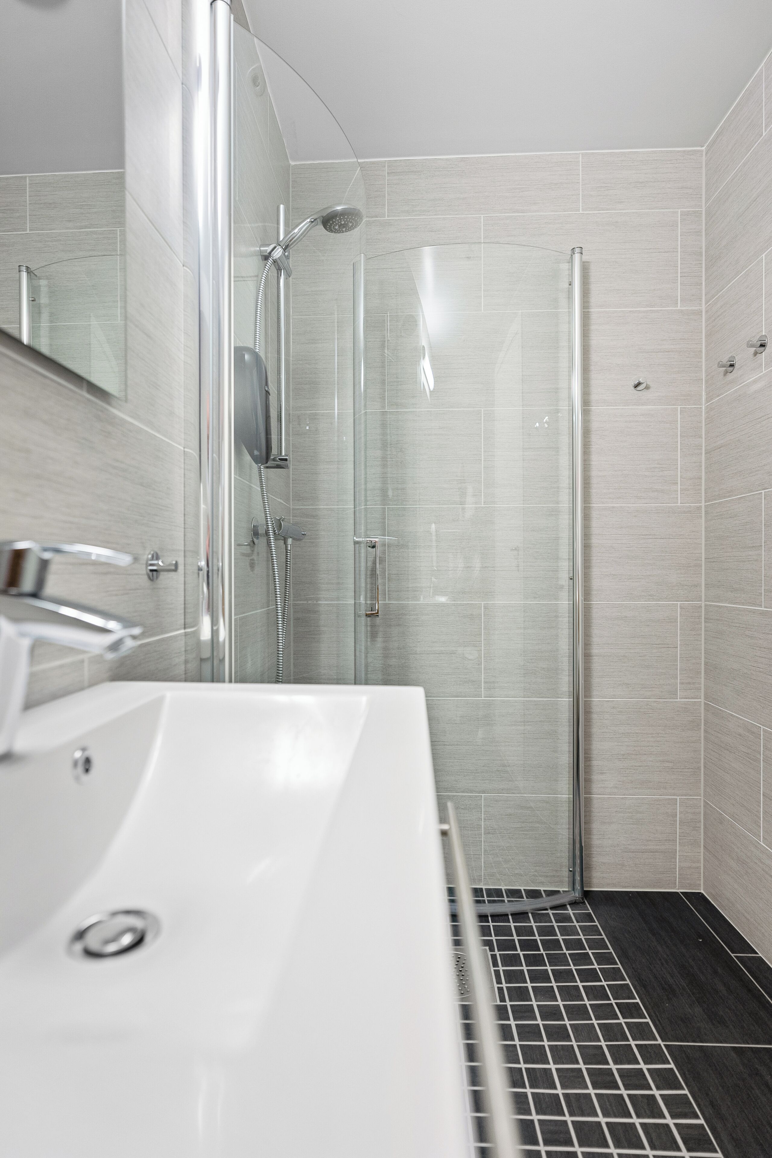 A modern bathroom with a glass shower enclosure, a white sink, and tiled walls.
