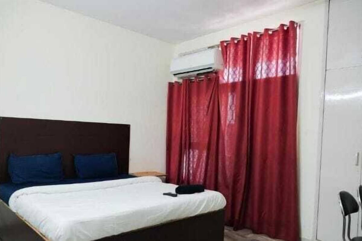 A bedroom with a bed, a headboard, a window with red curtains, and a wardrobe.