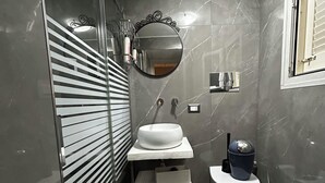 Un bagno moderno con box doccia in vetro, un lavabo bianco con piano in marmo e un water con coperchio blu.