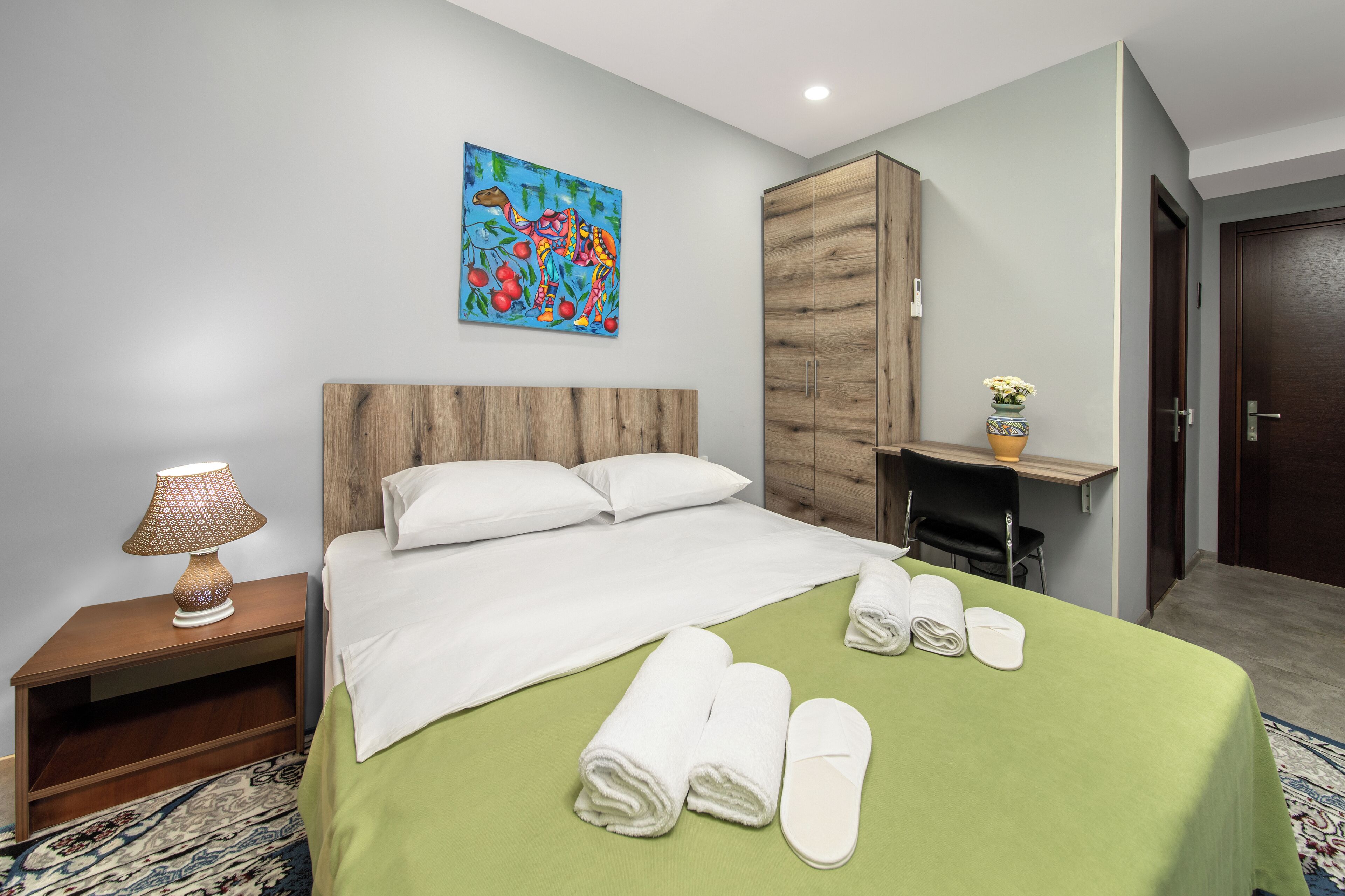 A hotel room with a bed, a nightstand, a desk, a cabinet, and a painting on the wall.