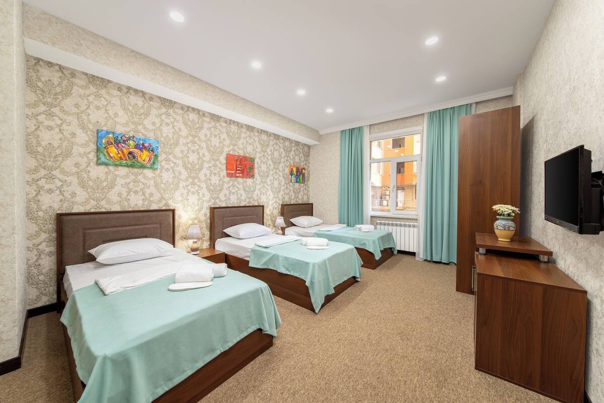 Habitación de hotel con tres camas, un televisor y un escritorio de madera.