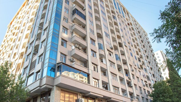 Un hotel alto de varios pisos con un diseño moderno, que cuenta con balcones en cada planta y una fila de coches aparcados al frente.