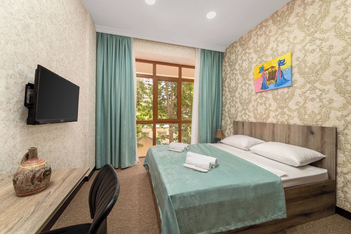 Una habitación de hotel con una cama, un escritorio con un televisor de pantalla plana, un florero y un cuadro en la pared.