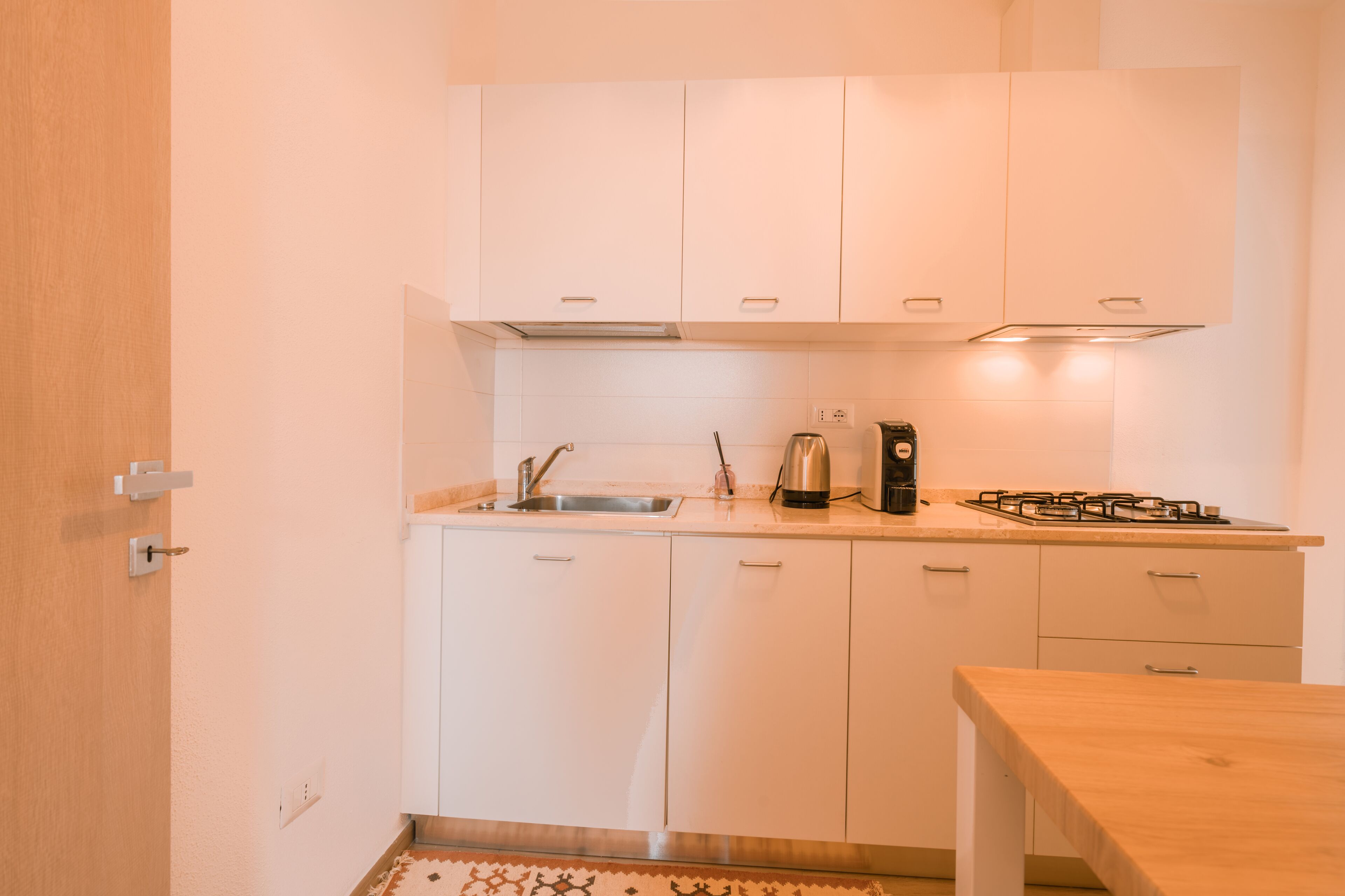A compact kitchen with white cabinets, a sink, a stove, and a small table.