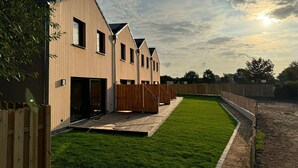 A row of modern wooden buildings with a well-maintained lawn and wooden fencing. - Great newly built house close to the beach (Insel Poel)
