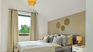 A bedroom with a bed, bedside tables, a nightstand, and a view of greenery outside. - Great newly built house close to the beach (Insel Poel)