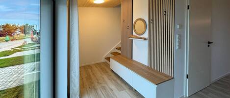 Un interior modern amb una escala de fusta, una porta blanca i vista a l'exterior.