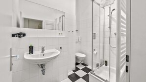 Un baño moderno con lavamanos blanco, espejo y cabina de ducha de vidrio.
