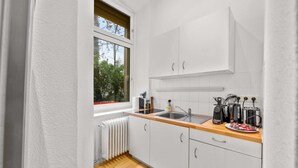Una cocina pequeña y moderna con armarios blancos, encimera de madera y ventana con vistas a la vegetación.